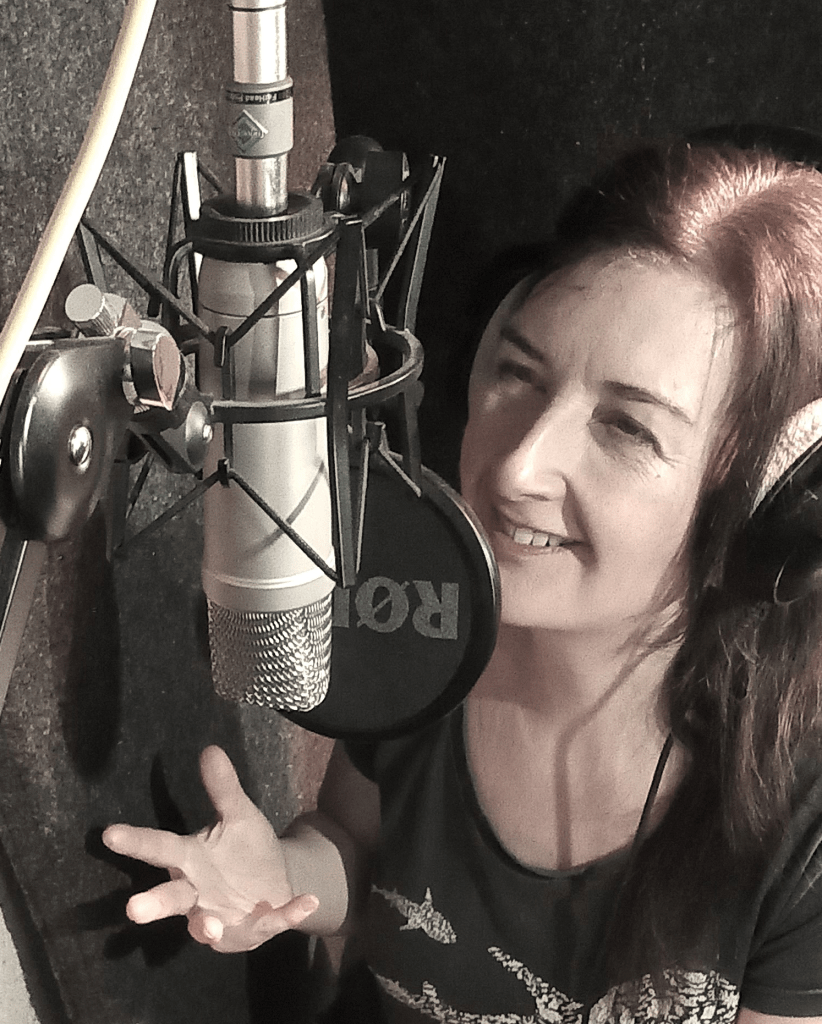 British female voiceover artist in headphones narrating into a rode microphone from a professional home studio